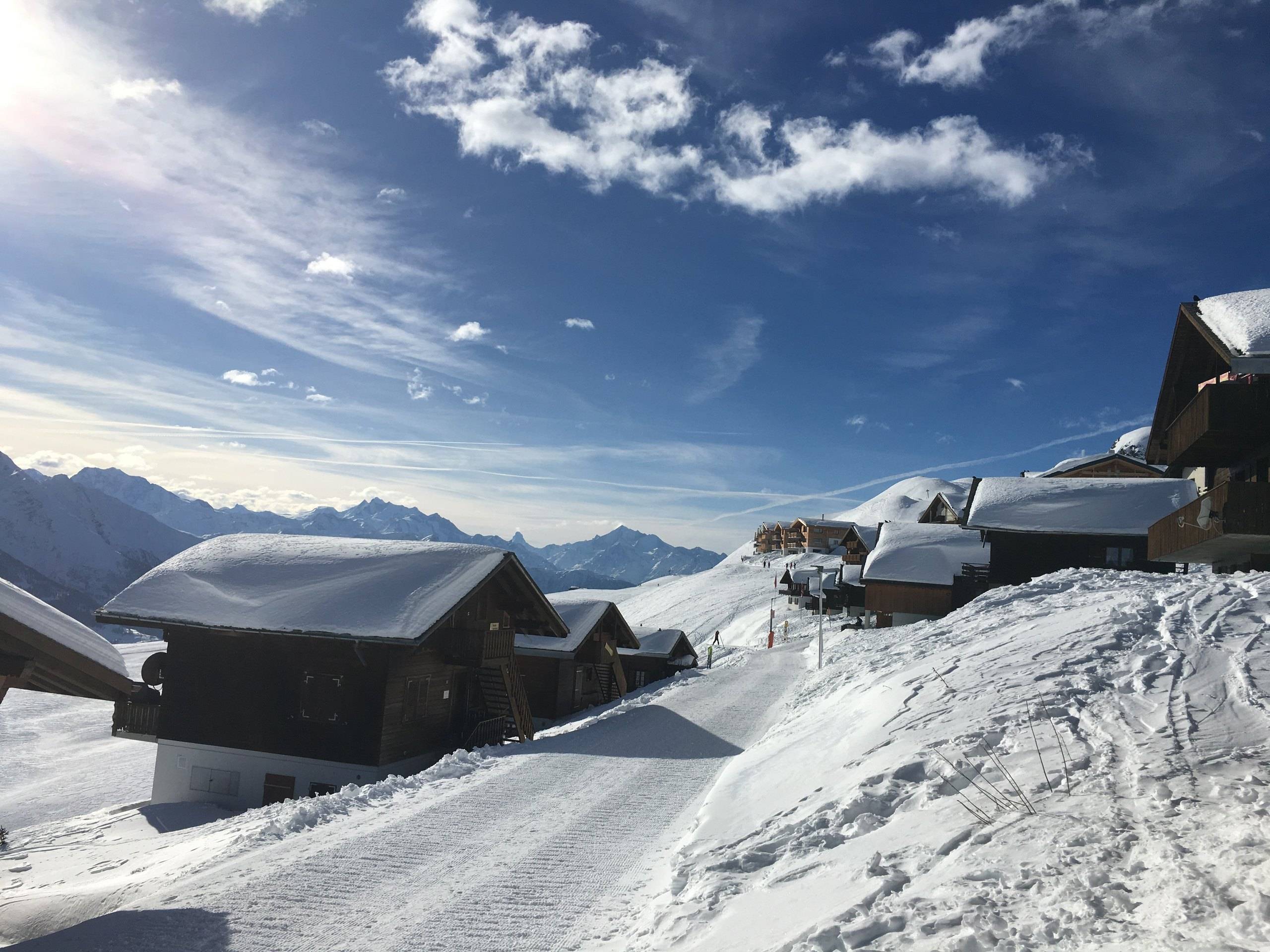 Verschneiter Winterweg auf dem Kühboden zwischen Chalets unter blauem Himmel