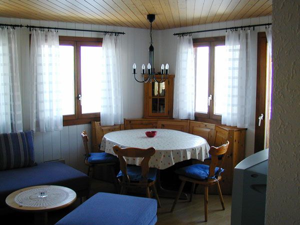 Wohnzimmer mit rundem Esstisch, Stühlen und Sitzbank vor zwei Fenstern